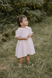 Young girl in a pink dress standing in a grassy field with trees in the background