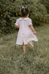 Young girl in a white dress walking through a grassy field with trees in the background