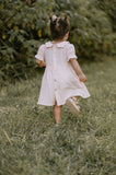 Young girl in a white dress walking through a grassy field with trees in the background
