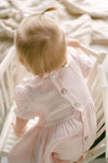 Baby in a pink outfit sitting on a white chair with a blurred background