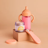 Pink sippy cup, jar, and spoon on a beige background