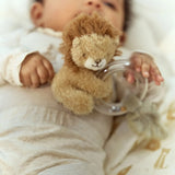 Baby holding a teddy bear and a glass bottle with a straw, wrapped in a blanket.