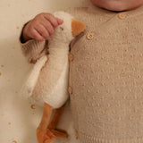 Child holding a plush toy resembling a duck, wearing a beige knitted sweater with buttons.