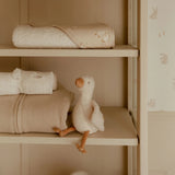 Shelf with folded towels and a plush goose toy in a neutral setting