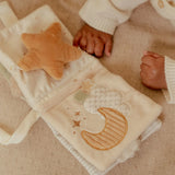 Baby blanket with star and moon design, child's hand holding a plush star toy.