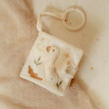 Embroidered baby rattle with duck design on a soft beige fabric background