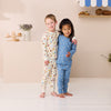 Two children wearing pajamas standing in a room with a shelf in the background.