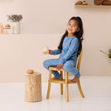 Young girl in blue pajamas sitting on a wooden chair in a room with a neutral color palette.