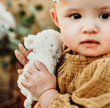 Child holding a white teddy bear with a blurred natural background