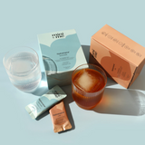 Cosmetic products including a box, glass of red liquid, and packets on a light blue background