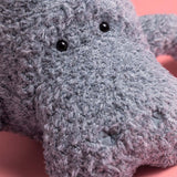 Close-up of a gray plush toy with black eyes on a pink background