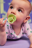 Baby with a green pacifier on a purple surface