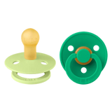 Two baby pacifiers, one green and one beige, on a white background.