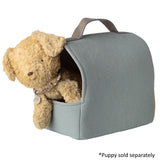 A plush tan teddy bear sits inside a small soft-sided pet bed with a handle. The bed is a muted sage green color, and a text note in the bottom right corner reads '*Puppy sold separately'.