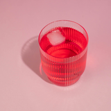 Clear glass with red liquid and ice cube on a pink background
