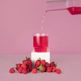 Red liquid being poured into a glass with strawberries on a pink background