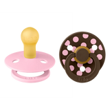 Two baby pacifiers, one pink and yellow, the other brown with pink polka dots, on a white background.