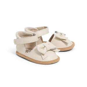 Pair of cream-colored baby sandals with bow details on a white background