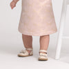 Child wearing a pink dress with bow patterns and beige shoes on a white background