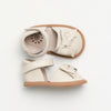 Pair of cream-colored baby shoes with brown soles on a light gray background