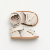 Pair of cream-colored baby shoes with brown soles on a light gray background