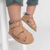 Children's feet wearing tan sandals with velcro straps on a light background