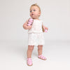 Baby in a white lace dress with pink sandals on a plain background