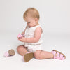 Baby sitting on a white background wearing pink checkered shoes.
