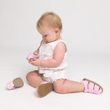 Baby sitting on a white background wearing pink checkered shoes.