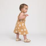 Baby wearing a mustard yellow dress with white floral patterns on a white background