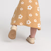 Child wearing a mustard yellow skirt with white floral patterns and matching shoes on a light gray background