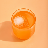 Glass of orange juice with a large ice cube on an orange background