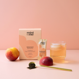 mini+me Hydramama peach numa product with a glass of peach juice and peaches on a pink background
