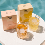 Two glasses of iced tea with 'mini + me' boxes on a white surface with a blue background.