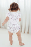 Child wearing a floral romper against a white curtain background