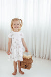 Young girl in a white floral dress holding a picnic basket against a white curtain background