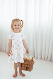 Young girl in a white floral dress holding a picnic basket against a white curtain background