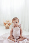 Baby wearing a pink floral romper sitting on a white blanket with a light background