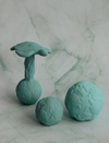Three teal massage balls with textured surfaces on a marble background