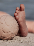 Close-up of a foot pressing into sand next to a beach ball.
