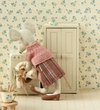 Stuffed animal in a dress standing next to a washing machine with floral wallpaper.