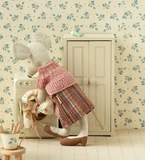 Stuffed animal in a dress standing next to a washing machine with floral wallpaper.