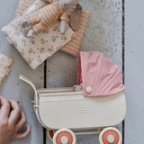 Small toy pram with a pink hat on a textured surface