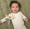 Baby lying on a green cushion holding a soft toy with a flower design.