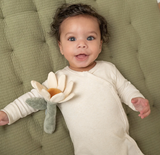 Baby lying on a green cushion holding a soft toy with a flower design.