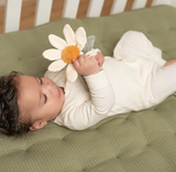 Baby lying on a green cushion holding a white flower toy.