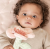Baby holding a soft toy with a pink and green design, wearing a beige knitted sweater.