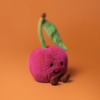 Pink knitted cherry with a stem on an orange background