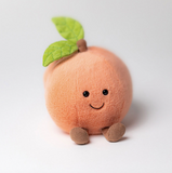 Plush toy shaped like a peach with a smiling face on a white background