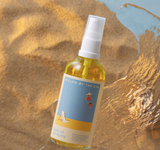 Bottle of 'Willow by the Sea' body oil for mums on a textured sand background